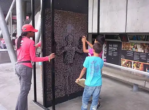 Un Pin Art grandeur nature à l'entrée du Parque Explora (en) (Colombie), où un enfant derrière pousse les clous.