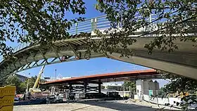 Le tablier de la nouvelle passerelle sur ses piles. Au premier plan, la passerelle piétonne en arc (août 2023).