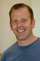 Photographie d’un homme souriant habillé en t-shirt.