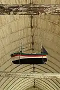 Vue en contreplongée d'une maquette suspendue à une poutre. Deux grands tangons en position levée de chaque côté du mât.