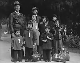 Des membres de la famille Mochida attendent le bus d’évacuation. Des étiquettes d’identification sont utilisées pour garder la cellule familiale intacte pendant toutes les phases d’évacuation. Mochida exploitait une pépinière et cinq serres sur un site de deux hectares dans le canton d’Eden, comté d'Alameda.