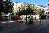 Photographie d'une place ombragée avec des maisons en arrière-plan.