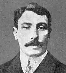 Photographie en noir et blanc d'un homme d'âge moyen avec une moustache. Il porte un costume et une cravate.