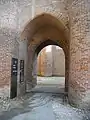 Photo couleur d'une porte à voûte en arc brisé en brique rouge. L'épaisseur des murs est visible, environ le double de la larguer de la porte.