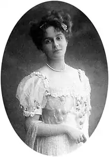 Portrait en pied d'une jeune fille aux cheveux attachés, vêtue d'une robe claire.