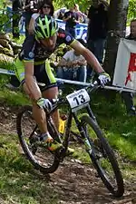 Homme descendant une pente à VTT, portant une tenue verte et noire.