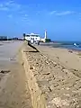 Vue des vestiges du rempart maritime ; au fond, le borj as-Sirat et le phare
