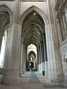Grande arcade de pierre donnant accès à des bas-côtés s'étendant, au loin, jusqu'à une verrière.