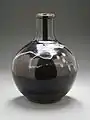 Photo couleur montrant une bouteille en terre cuite sur fond gris.