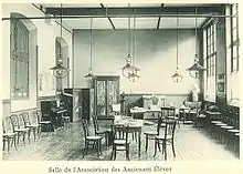 Photographie de la salle de l'AAE à la fin du XIXe siècle : il y a des meubles, un piano et un buste de Molière.