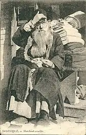 photographie noir et blanc : un homme barbu devant des rouleaux de tissu.