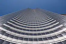 Photographie du bâtiment depuis le bas jusqu'au ciel. Il forme une sorte de gouttière ouverte concave.