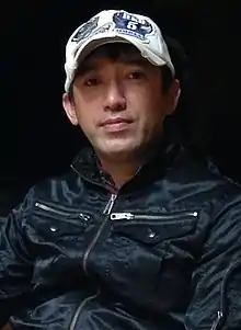 Photo en couleur d'un homme asiatique portant un blouson noir et une casquette blanche.