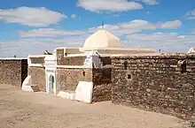 Un bâtiment en pierre sèche, avec une coupole blanche au sommet et des parements blancs, notamment autour d'une porte d'entrée.