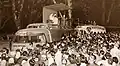 Le car podium lors d'une étape du Tour de France. Des artistes Pathé-Marconi se produisent sur la scène du véhicule située sur le toit, vers 1955
