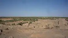 dans des tons ocres, sur trois plans, un sol de pierre, un village de terre de même couleur, et des arbres verts éparses