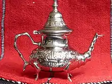 Théière décorée argentée sur fond de rideau rouge.