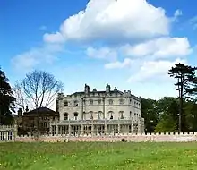 Photo d'un grand bâtiment aux murs blancs et aux grandes fenêtres au milieu d'un parc avec de grands arbres