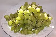 Photographie montrant une grosse grappe de sultanine ; les grains ovales sont vert-jaune. Leur pruine a partiellement été enlevée par le lavage.