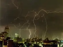 Ciel nuageux dans lequel se trouvent des dizaines d'éclairs, au-dessus d'une ville.