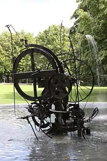Une fontaine en métal au milieu d'une esplanade engazonnée