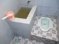 Cuvette pour s'accroupir (Indonésie). A gauche, la cuvette à eau et la casserole pour le nettoyage anal.