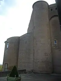 Photo couleur d'une double tour en brique rouge massive. La partie gauche a été réduite en hauteur, laissant un mur tronqué oblique. À droite, la hauteur initiale subsiste et montre un mâchicoulis appuyé sur les tourelles d'angles.