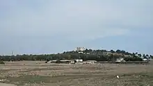 Vue d'une plaine avec au fond une colline avec un grand édifice religieux et sur la gauche un minaret à l'arrière-plan.