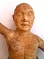 Photographie en couleurs représentant une statuette à la tête chauve et au torse nu.