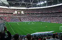 Vue à mi-hauteur depuis les tribunes d'un stade avec ses tribunes remplies avec un match en cours.