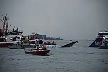 L'avion, au centre de l'image, à peine visible à mesure qu'il coule dans le fleuve, est entouré par plusieurs navires de secours.