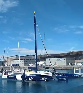 Vu en entier, de trois quarts avant, trimaran bleu et blanc amarré au ponton.