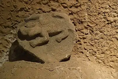 Pierre sculptée beige posée sur un tas de terre posée sur un mur de terre.