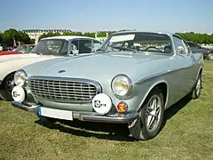 Une Volvo 1800 E avec des Cibié fixés sur le pare-chocs.