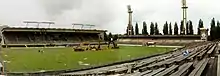 Photographie d'un stade de football vu d'un angle des tribunes, des engins de chantier sont au centre du terrain.