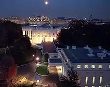 Entrée principale de l'aile Ouest au premier plan à droite et la résidence au fond, au mur éclairé. La photo est prise depuis le Old Executive Office Building.