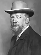 Portrait photographique en noir et blanc d'un homme à la barbe grisonnante coiffé d'un chapeau gris clair.