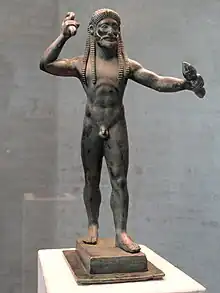 Statue noire d'un homme debout tenant des pics dans ses mains.